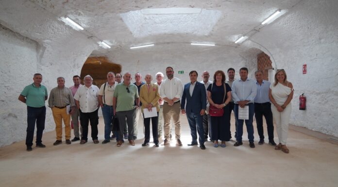 Tomelloso acoge el pleno del CRDO La Mancha. La asamblea posan en la cueva del mercado de abastos junto a represetantes del ayuntamiento de Tomelloso